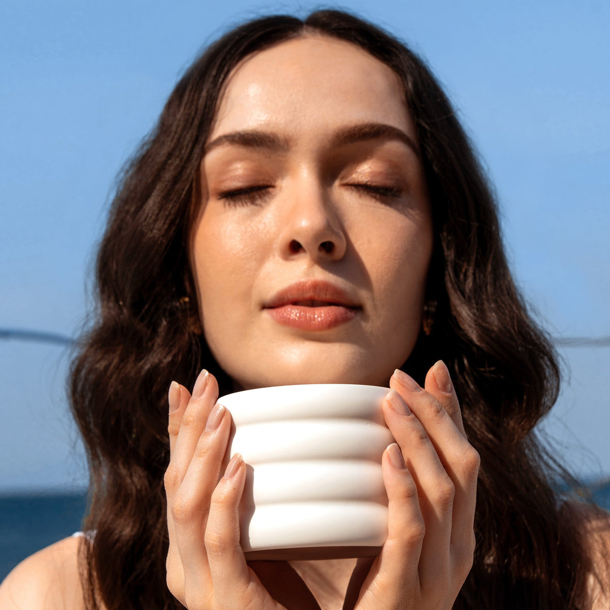 White ribbed ceramic candle with lit wick held close to face