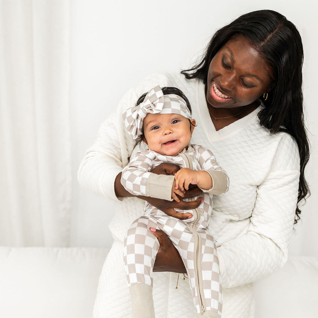 Baby in checkered hooded zippy suit with front zipper and footed legs; beige and white