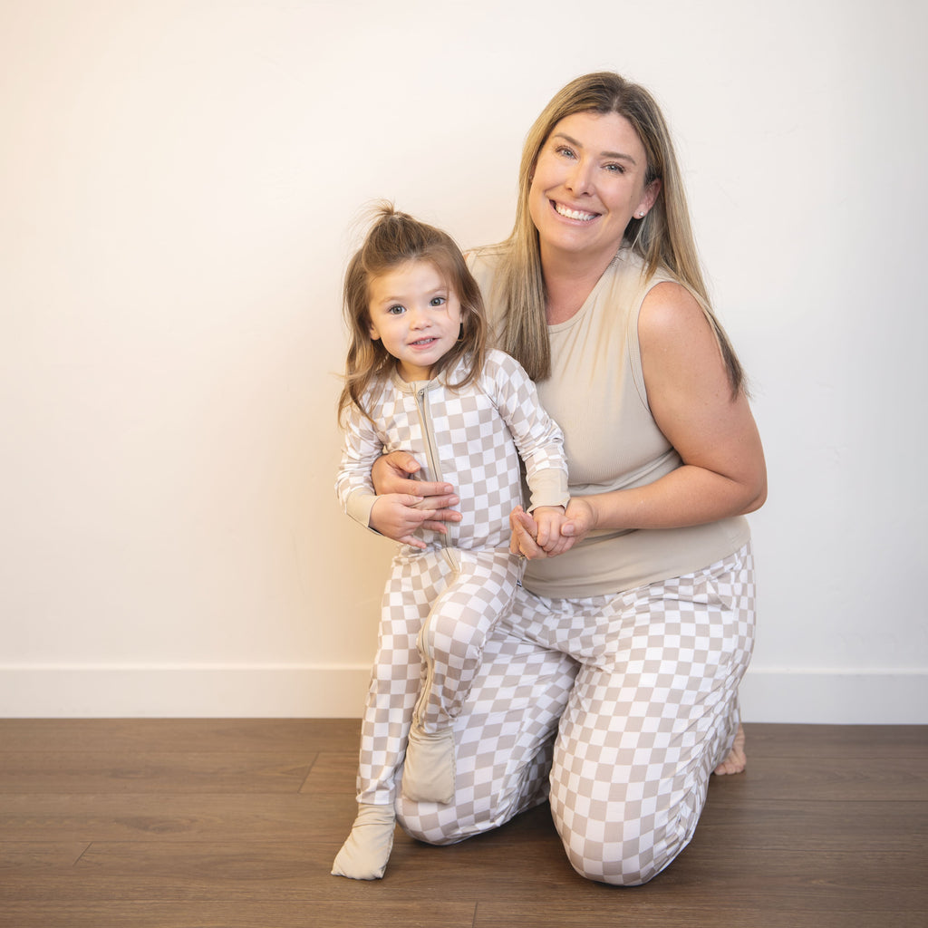 Adult and child wearing matching checkered zippy coveralls with front zippers; beige and white