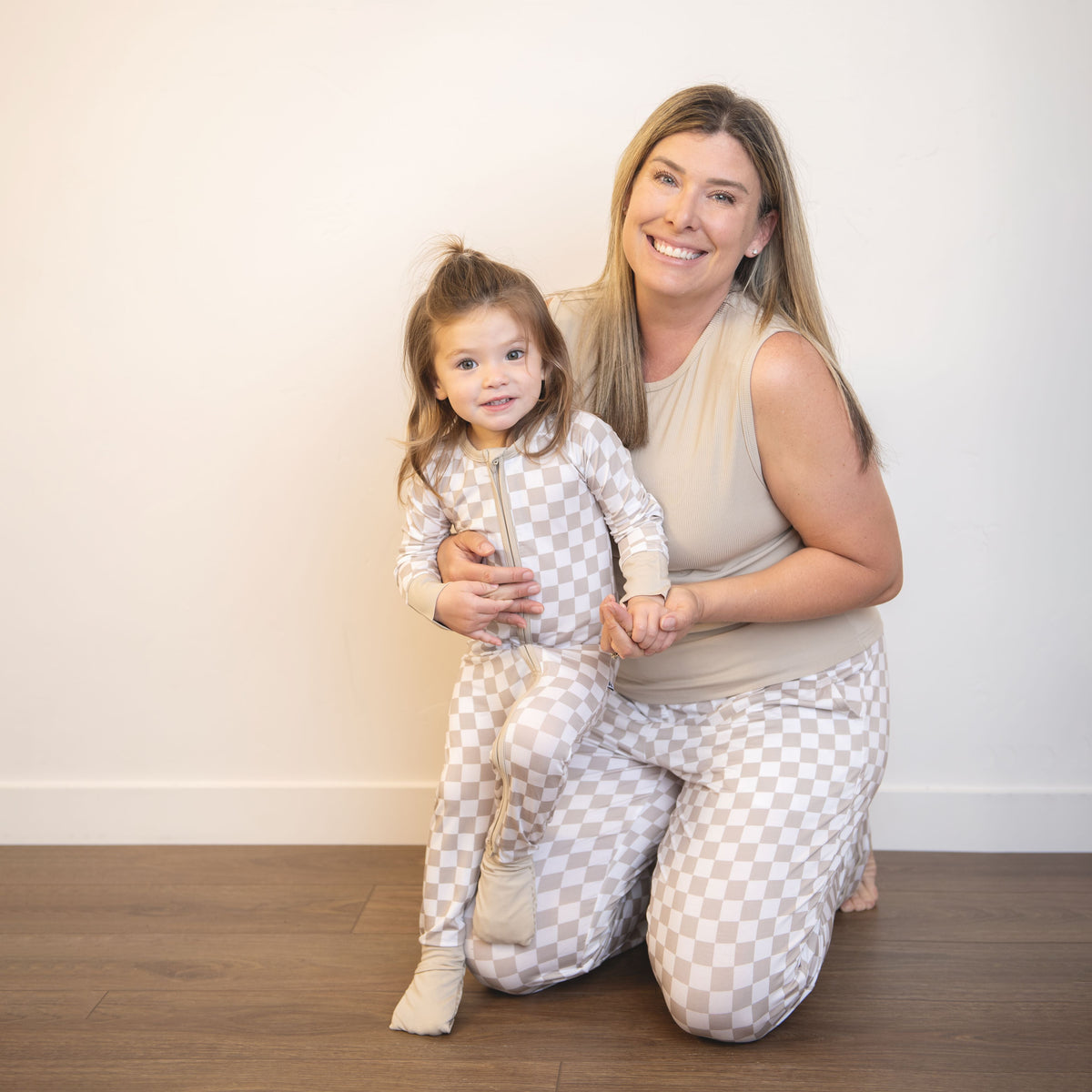 Adult and child wearing matching checkered zippy coveralls with front zippers; beige and white