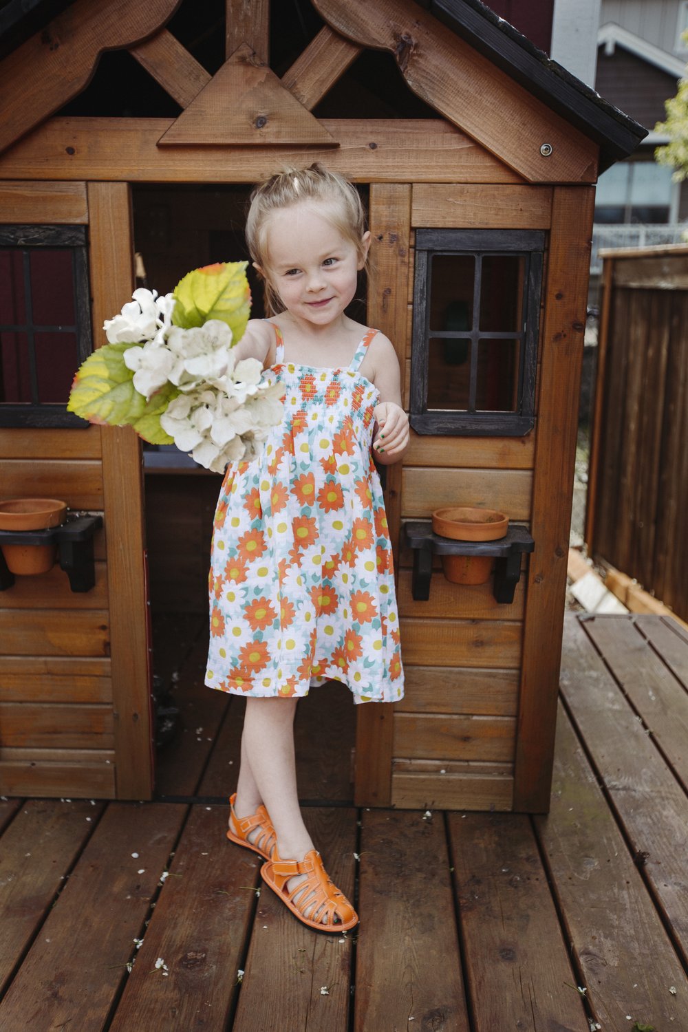 Orange kids sandals on a child near a wooden house, open-toe with hook straps