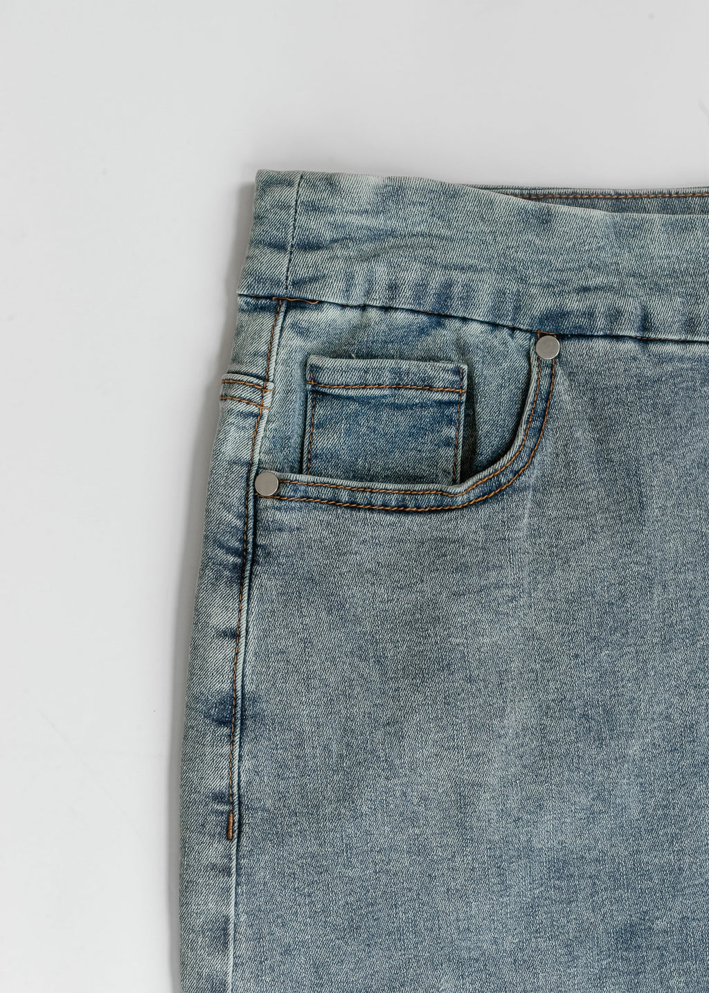 Close-up of light blue denim midi skirt front: curved pocket and contrast stitching