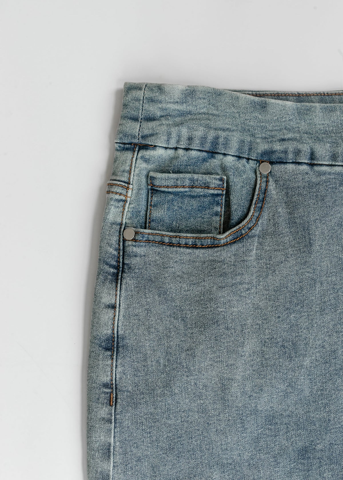 Close-up of light blue denim midi skirt front: curved pocket and contrast stitching