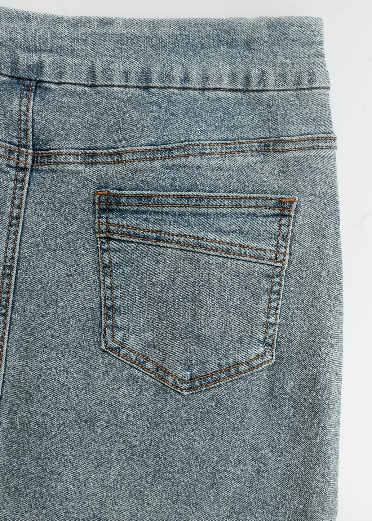 Close-up of back pocket and waistband of light blue washed denim midi skirt