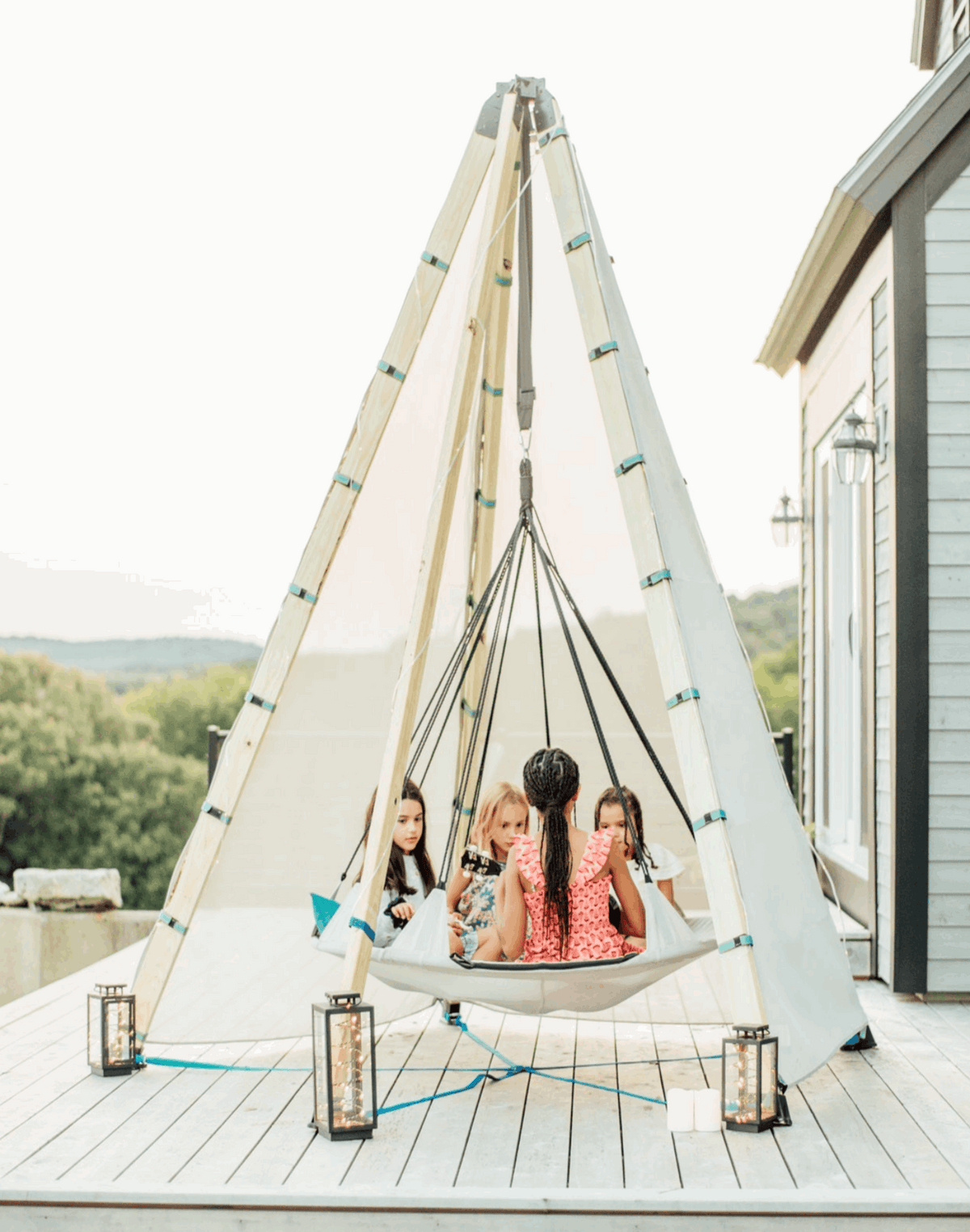Off-white tipi play tent on patio with wooden poles and green-trim ties