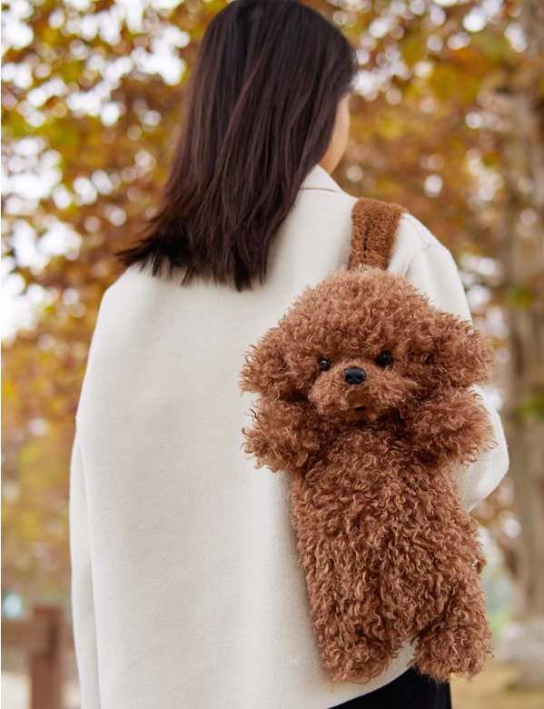 Brown plush puppy backpack with stitched eyes and nose, worn over the shoulder