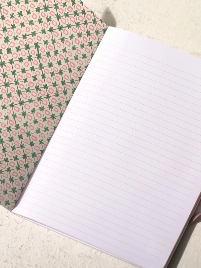 Notebook open to lined pages with decorative floral cover backing, sewn binding edge
