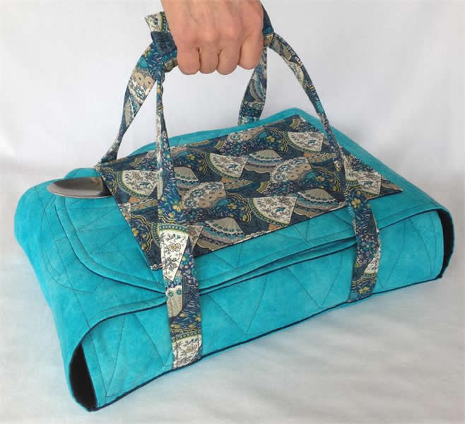 Quilted turquoise casserole carrier with top flap and patterned fabric handles
