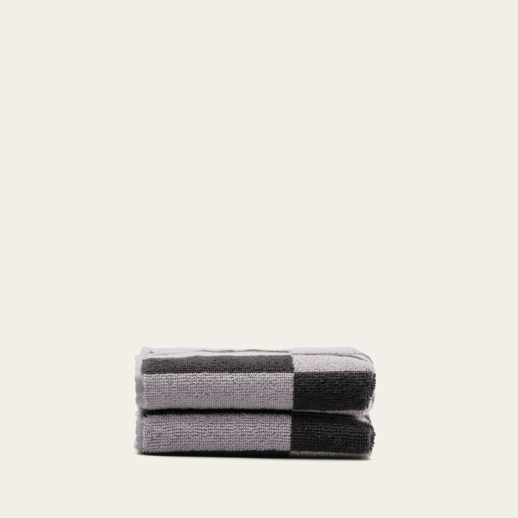 Stack of folded charcoal-and-lilac checkered towels on a light background.