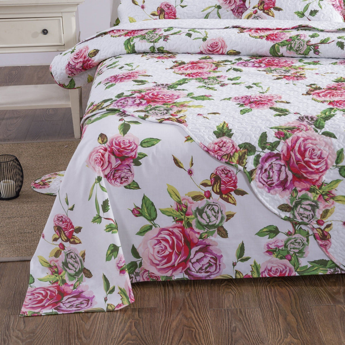 White sheet with pink rose and green leaf floral print, draped across bed
