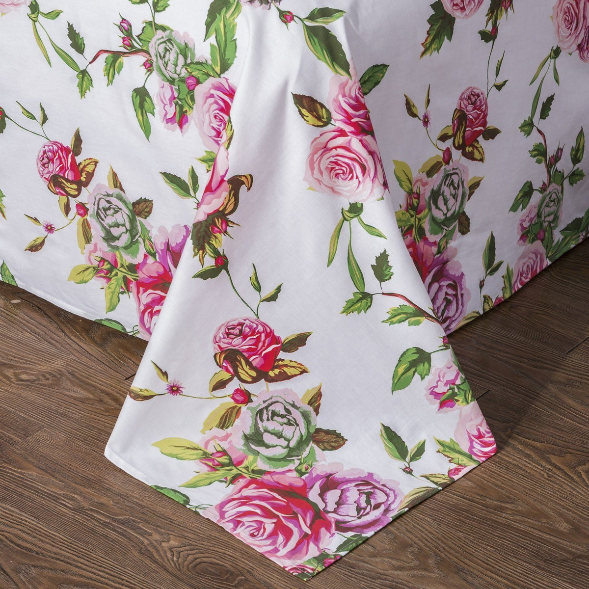 White floral sheet with pink roses and green leaves, folded corner on wood floor