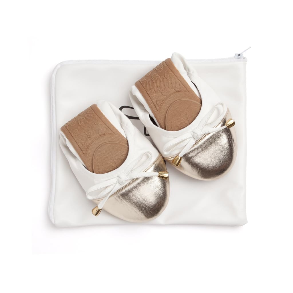 Pair of white flats with metallic toe caps in white dust bag, bow ties visible.