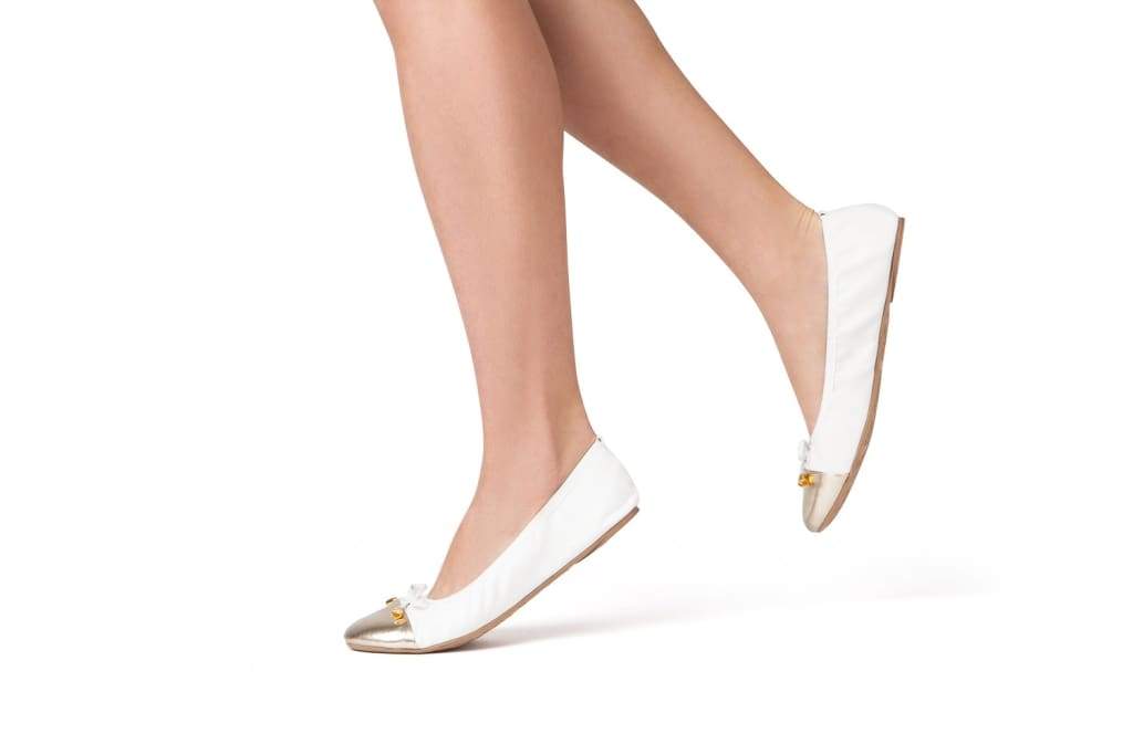 White flats with metallic toe cap and bow tie, shown from side on model.