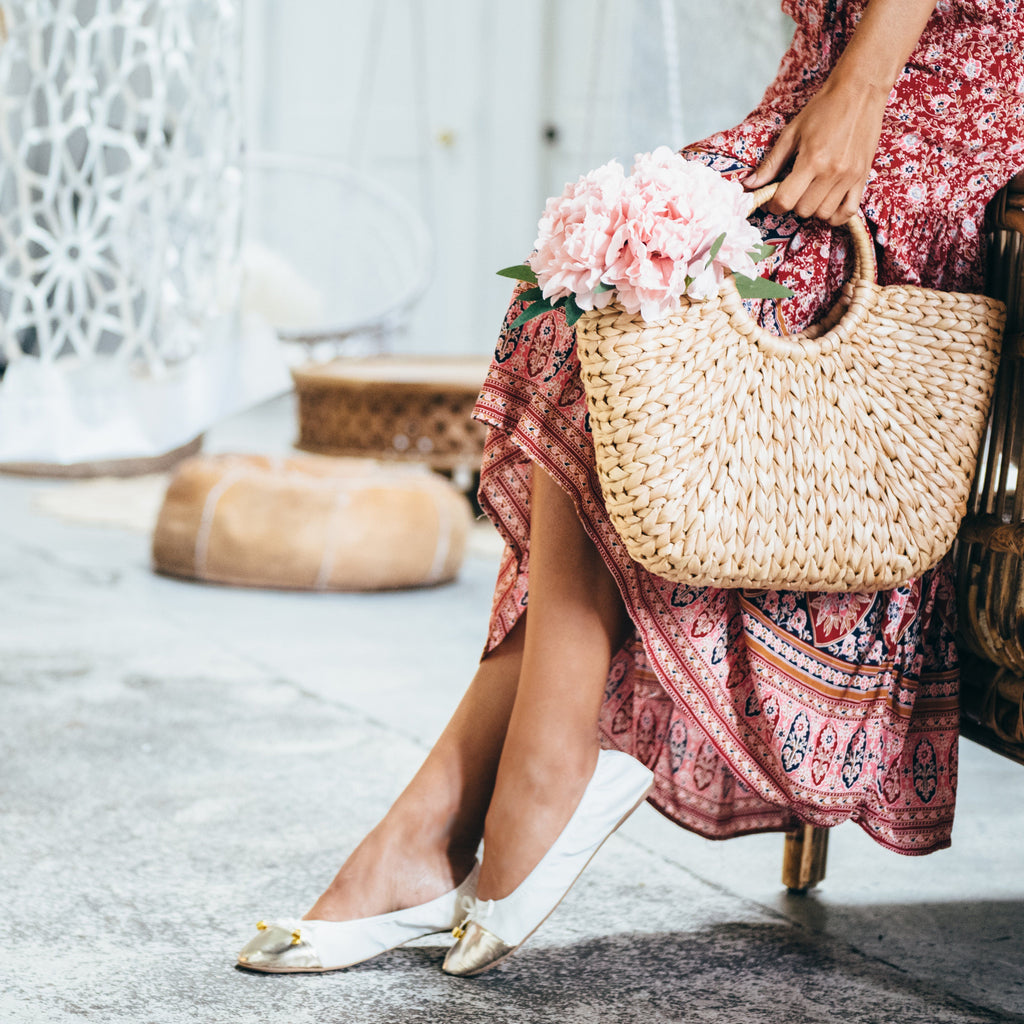 White flats with metallic toe cap and gold bow detail, worn with a skirt.