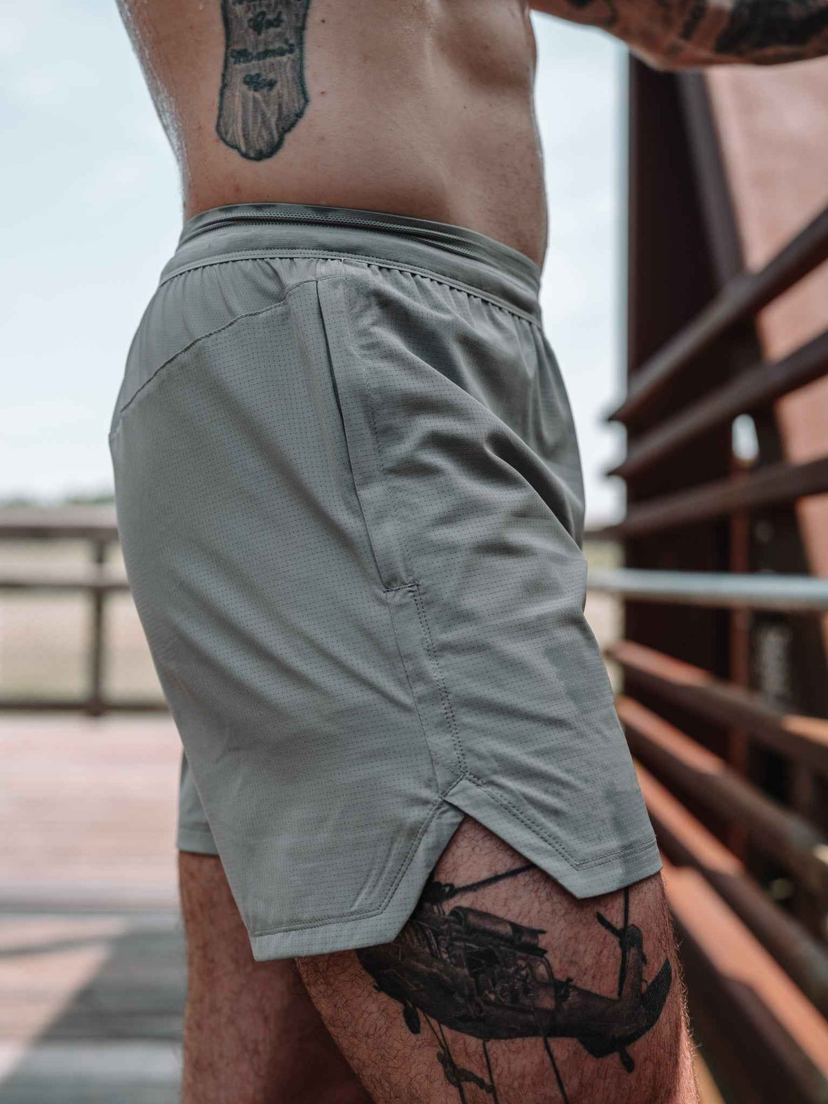 Gray athletic shorts on model with elastic waistband and stitched side pocket opening.