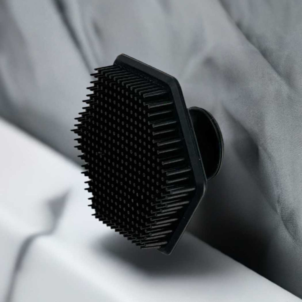 Black silicone cleansing brush with dense bristles, resting on a fabric surface