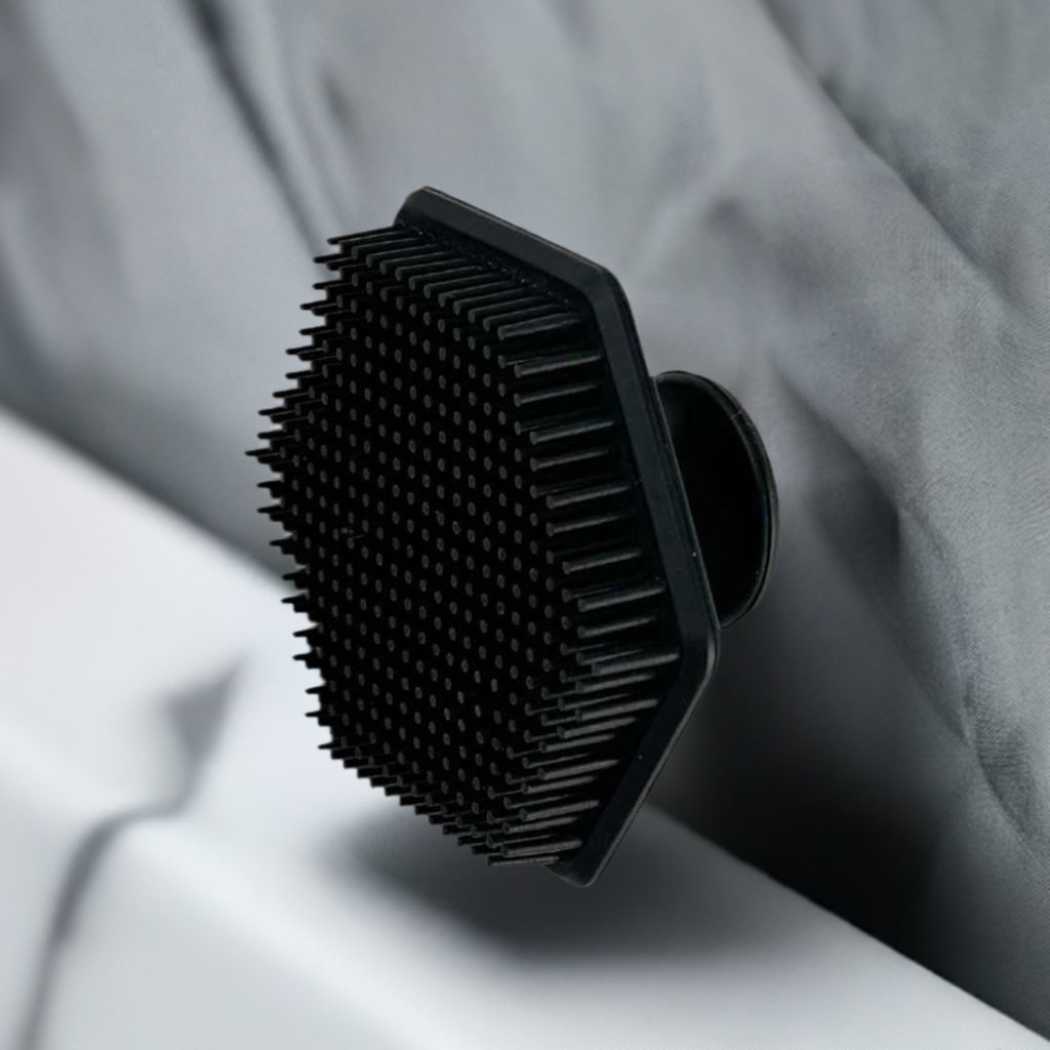 Black silicone cleansing brush with dense bristles, resting on a fabric surface