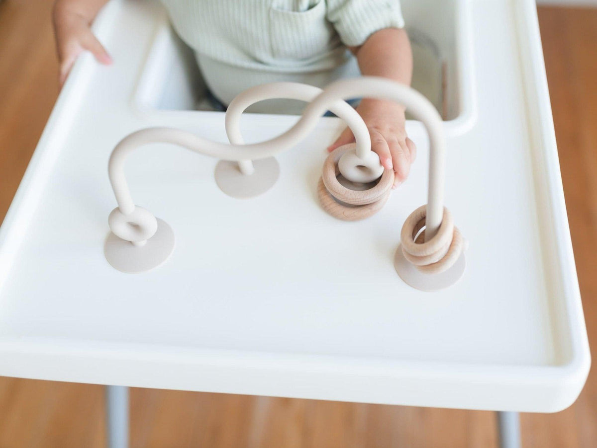 Silicone highchair toy with cream arch and two dangling ring pieces on tray