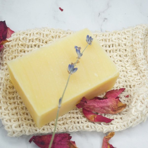 Beige sisal soap bag holding a yellow soap bar with dried flowers visible.