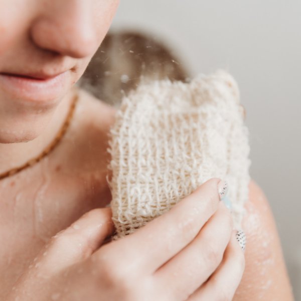 Hand holding a beige woven sisal soap bag with soap suds on mesh.