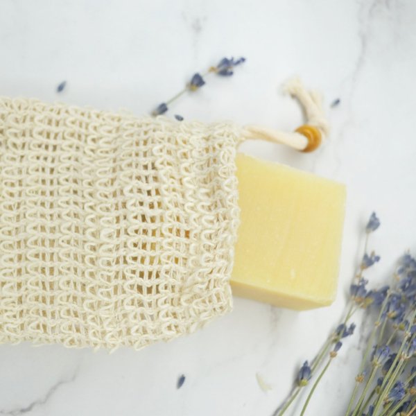 Beige woven sisal soap pouch with yellow soap bar and open top drawstring.