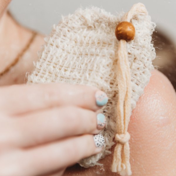 Beige sisal soap bag with wooden bead and cotton drawstring, held in hand.