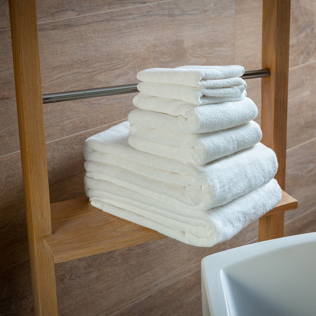 Stack of white bath towels folded on a wooden shelf, plush towel set