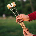 Metal s'mores roasting sticks with wooden handles, holding marshmallow for roasting