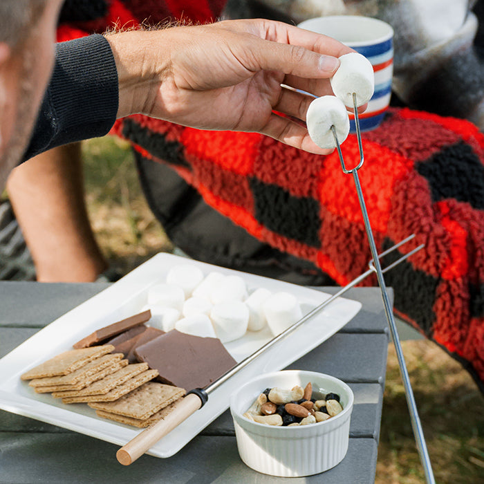Roasting stick holding marshmallow above s'mores tray with graham crackers