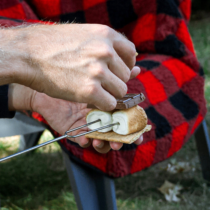Hand toasting s'mores on a roasting stick with marshmallow and graham cracker