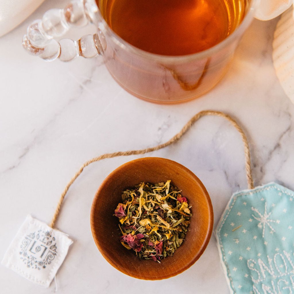 Wooden bowl of loose herbal tea leaves with dried petals on marble