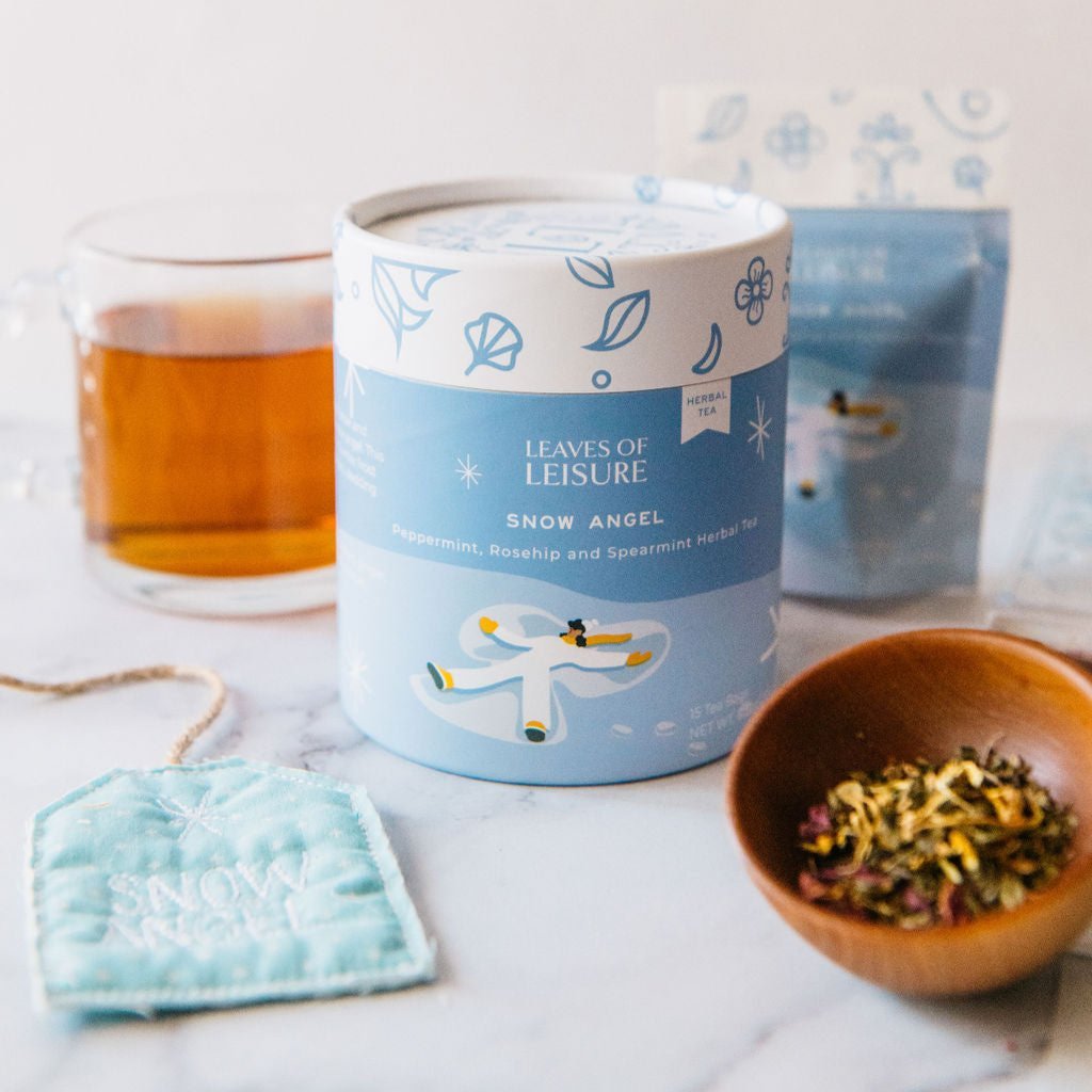 Round blue herbal tea tin with brewed amber tea and wooden bowl of leaves