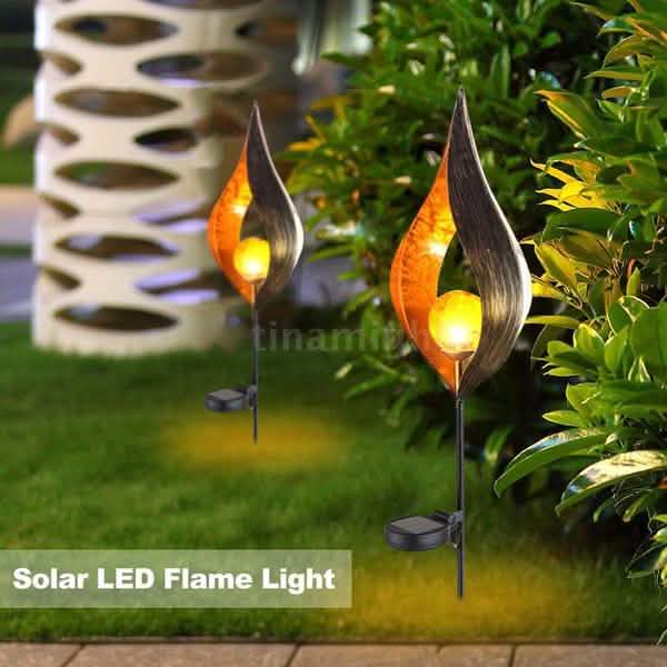 Pair of solar LED flame stake lights glowing near garden bushes and path area