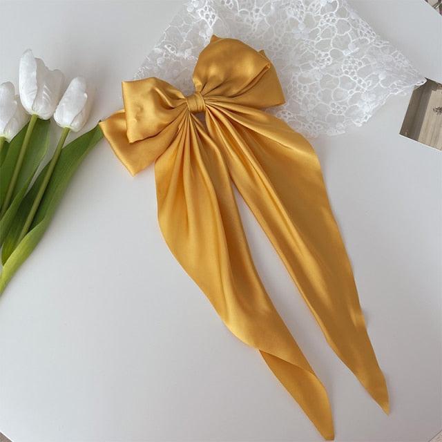 Gold satin bow hair clip with layered bow center and long ribbon tails