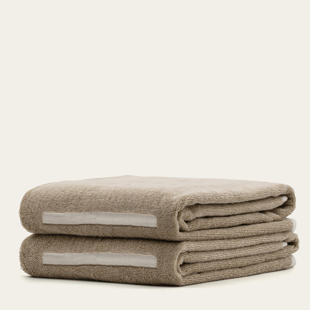 Two folded tan cotton towels with ecru stripe inserts, plush textured loop pile.