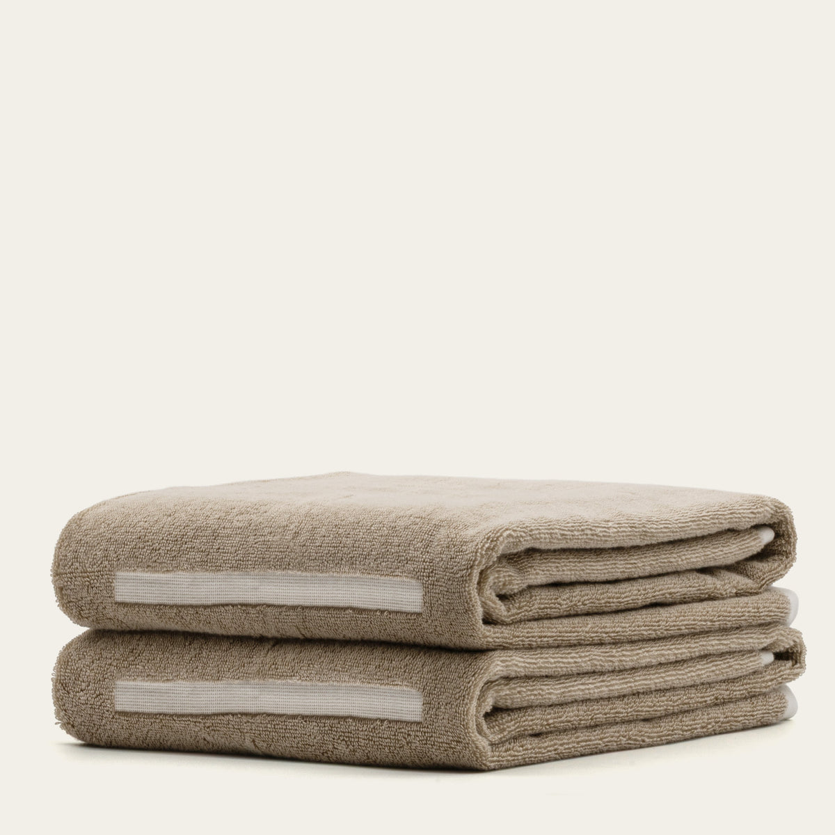 Two folded tan cotton towels with ecru stripe inserts, plush textured loop pile.