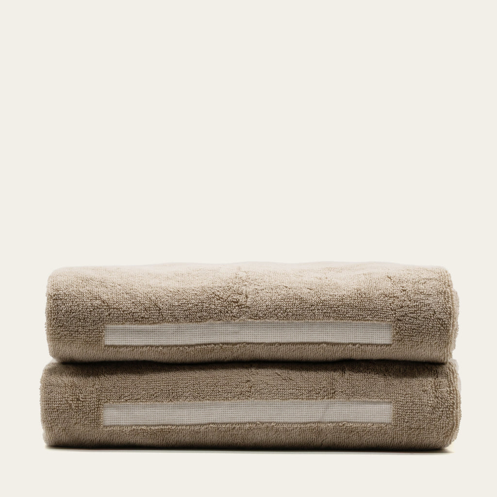 Tan cotton bath towel with ecru stripe accents, folded and stacked