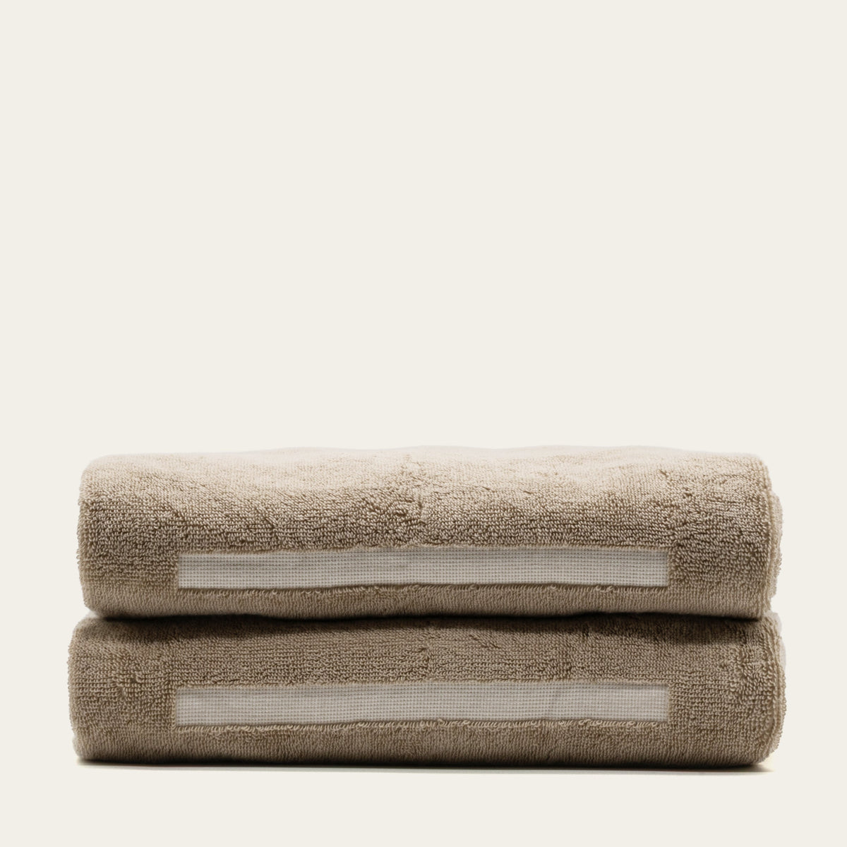 Tan cotton bath towel with ecru stripe accents, folded and stacked