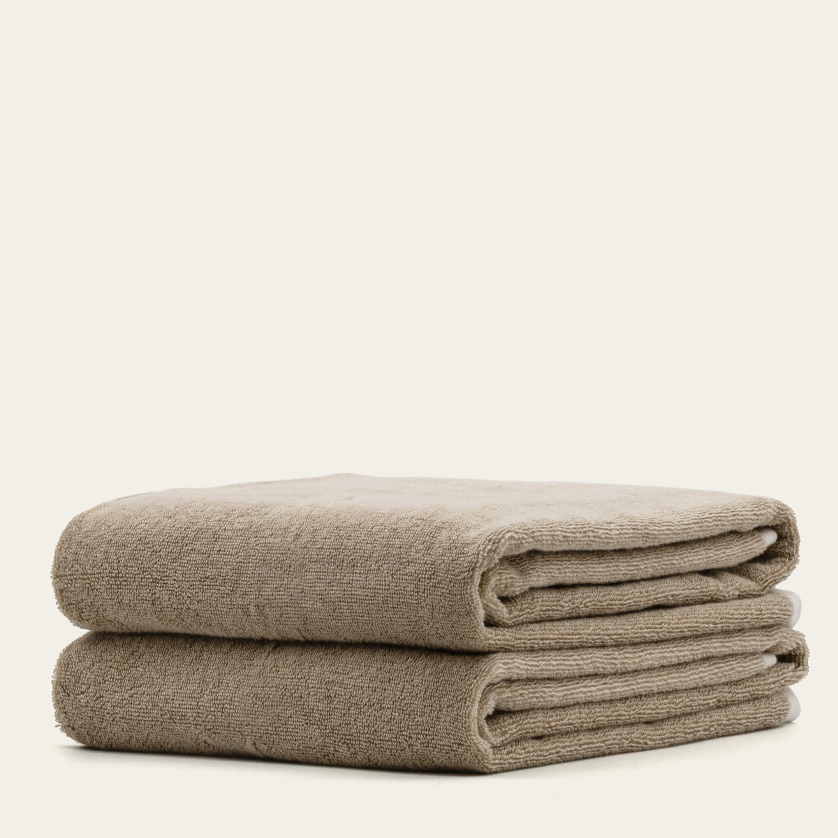 Tan cotton bath towels stacked with ecru stripe detail, folded