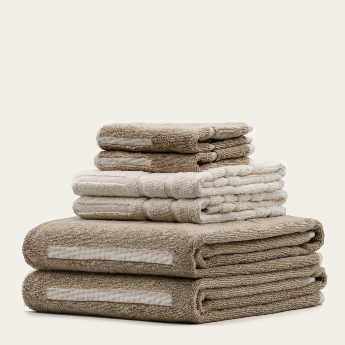 Mixed ecru and tan cotton towel stacks with stitched stripe bands and thick pile.