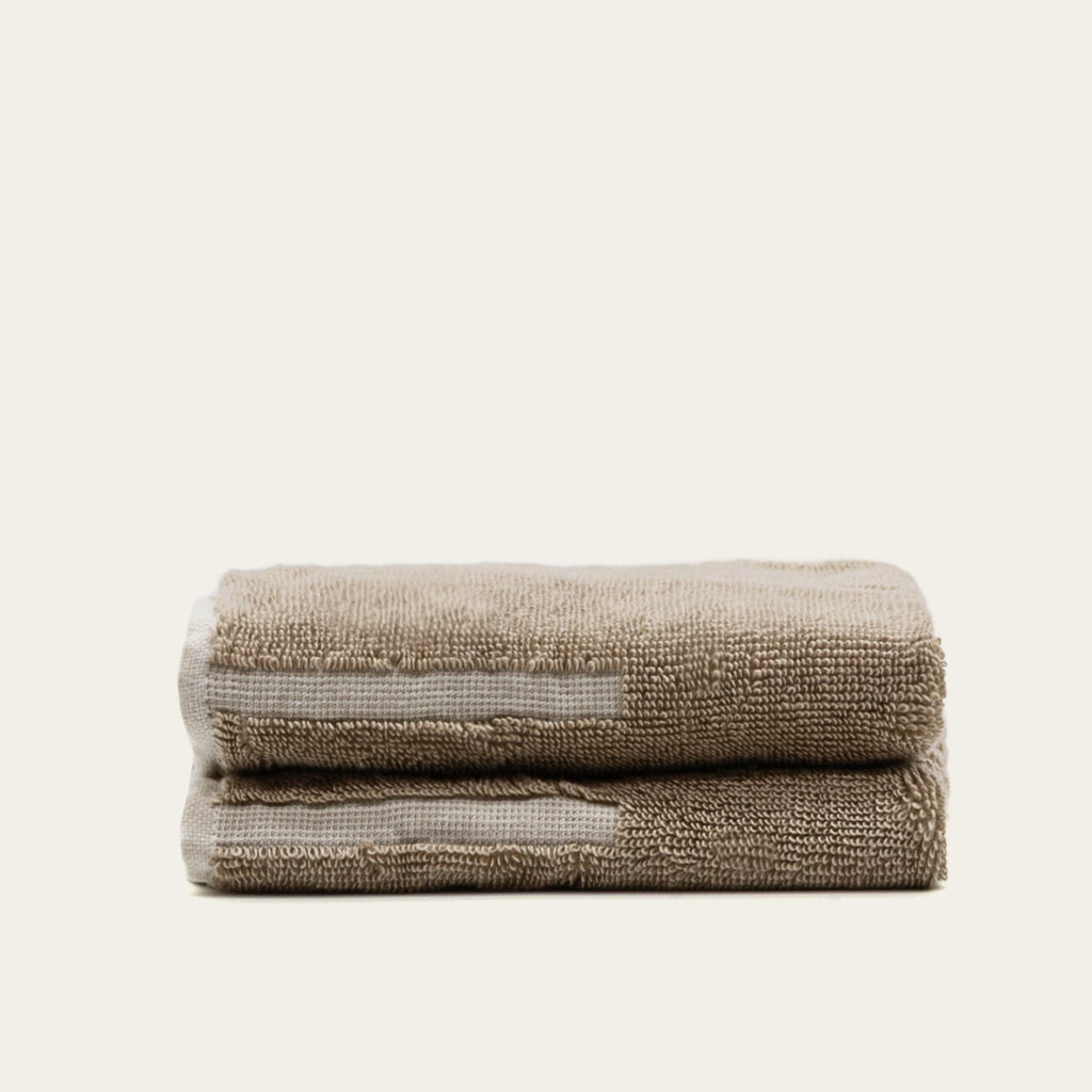 Folded tan cotton towel with ecru stripe accent, thick textured loop pile.