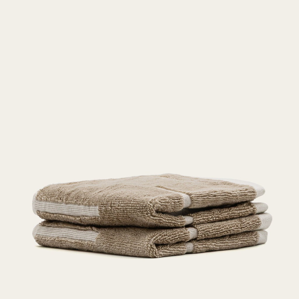 Stack of tan and ecru cotton towels with striped accent bands and textured weave.