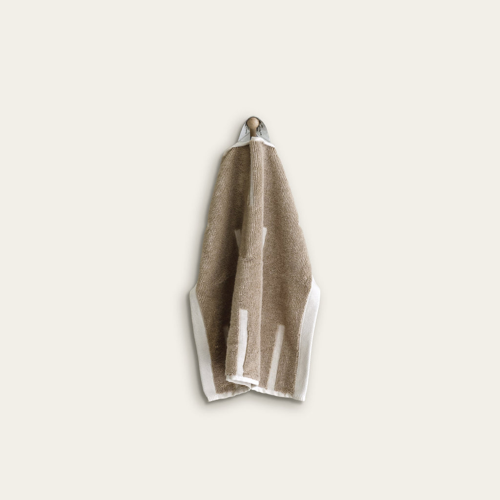 Tan cotton washcloth with ecru border stripes, neatly folded with hanging loop