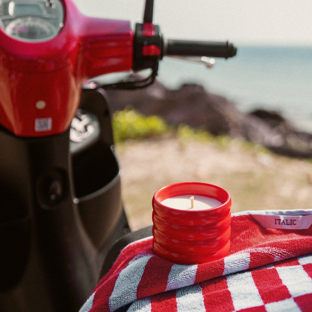 Red ribbed ceramic candle with lit flame on a checkered cloth