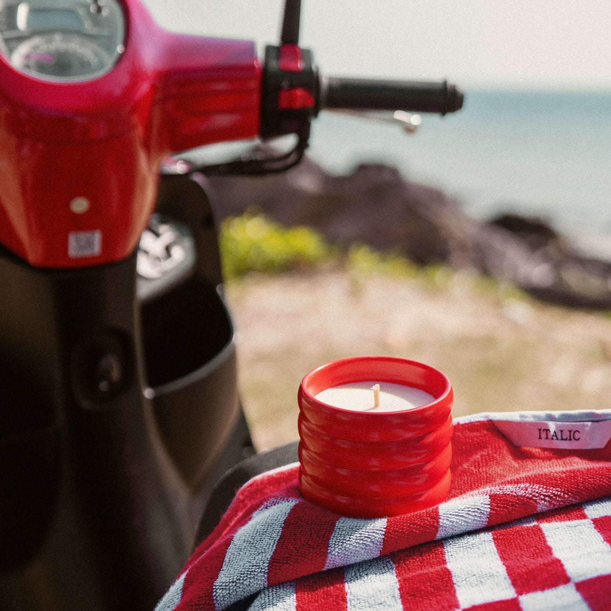 Red ribbed ceramic candle with lit flame on a checkered cloth