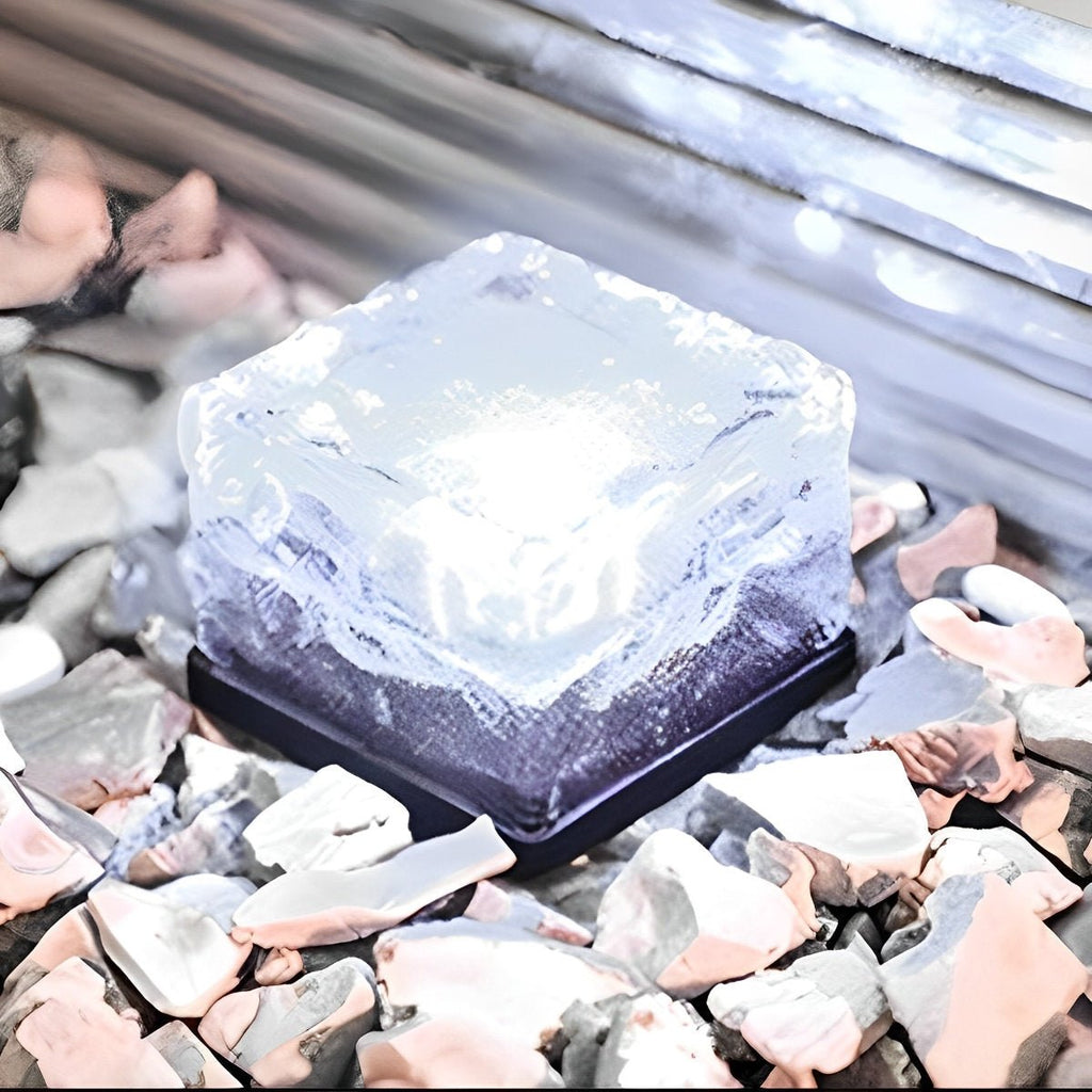 Solar LED ice brick light glowing cool white with blue tint, square on gravel