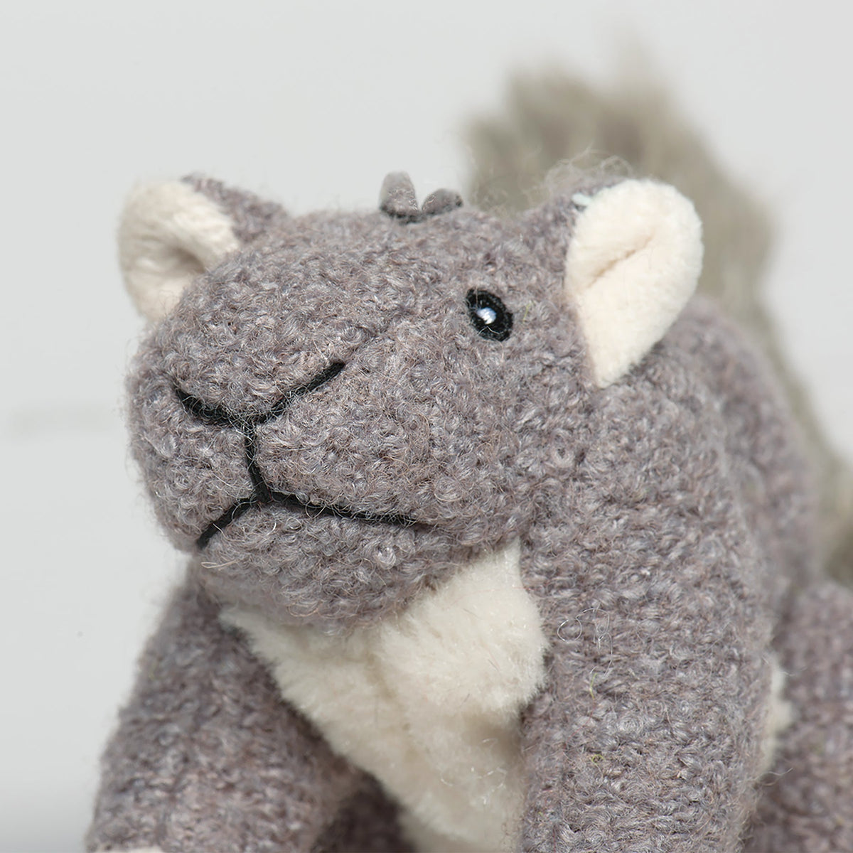 Gray-brown plush squirrel face with black nose, embroidered eyes, and cream muzzle