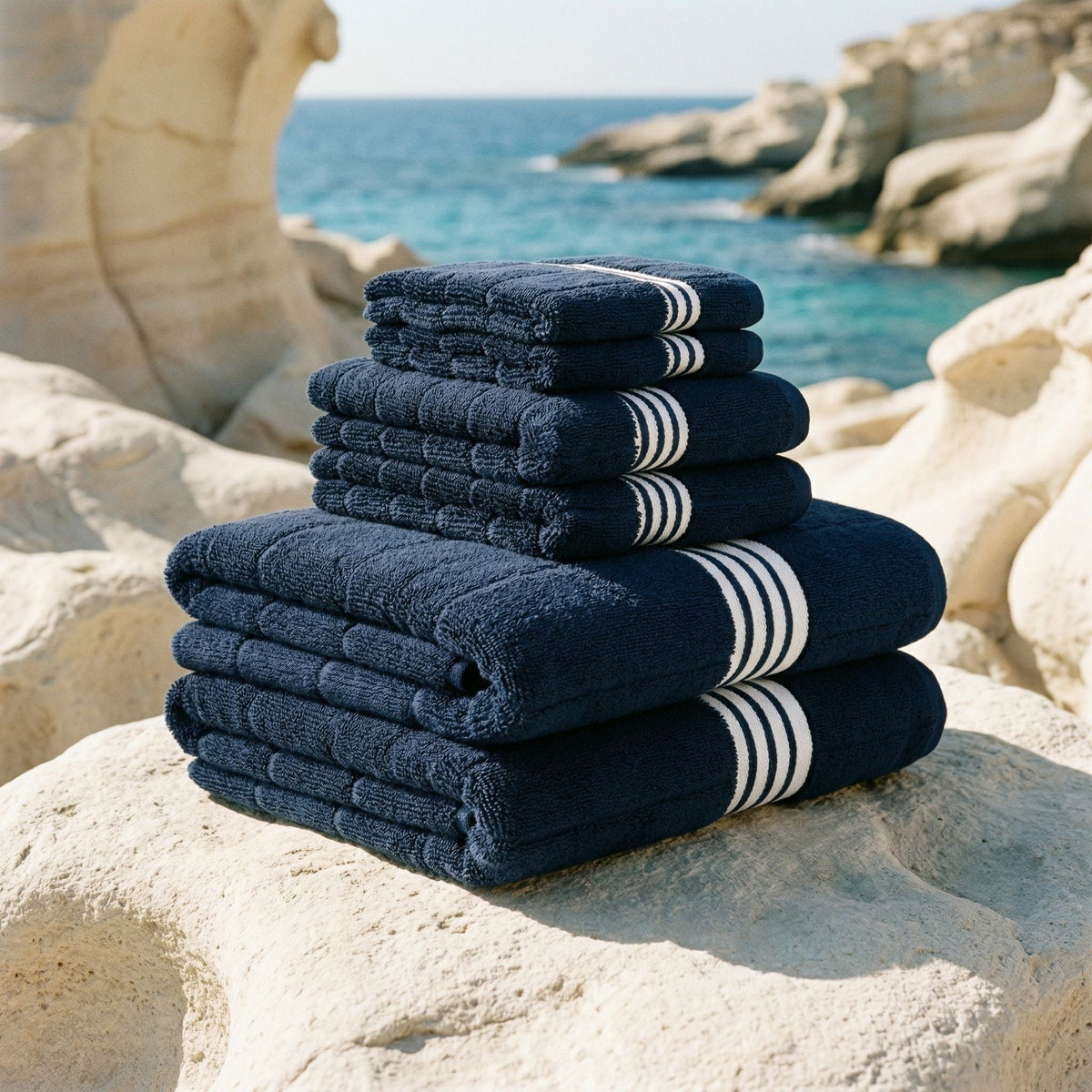 Stack of navy cotton towels with thick white stripe bands, folded and ready to use.