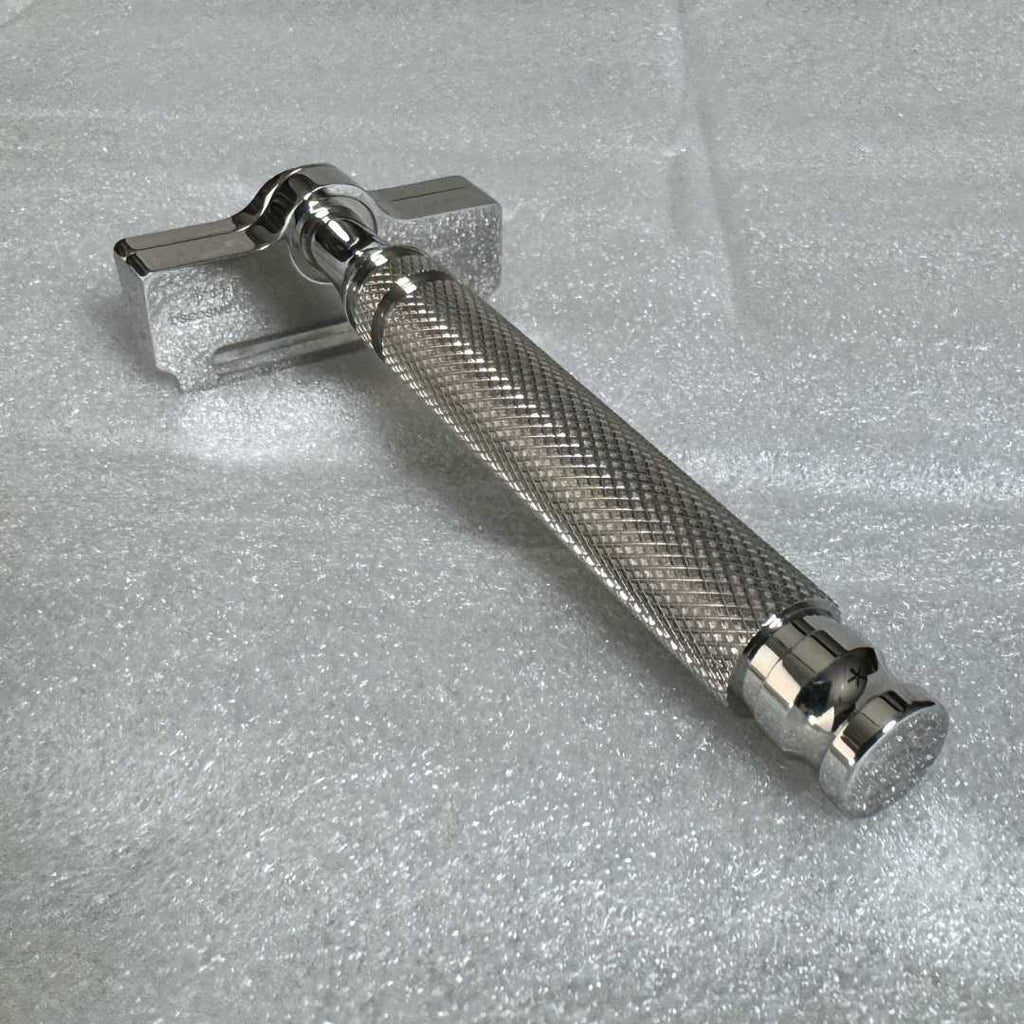 Safety razor lying flat: chrome head, textured grip, and knurled handle end