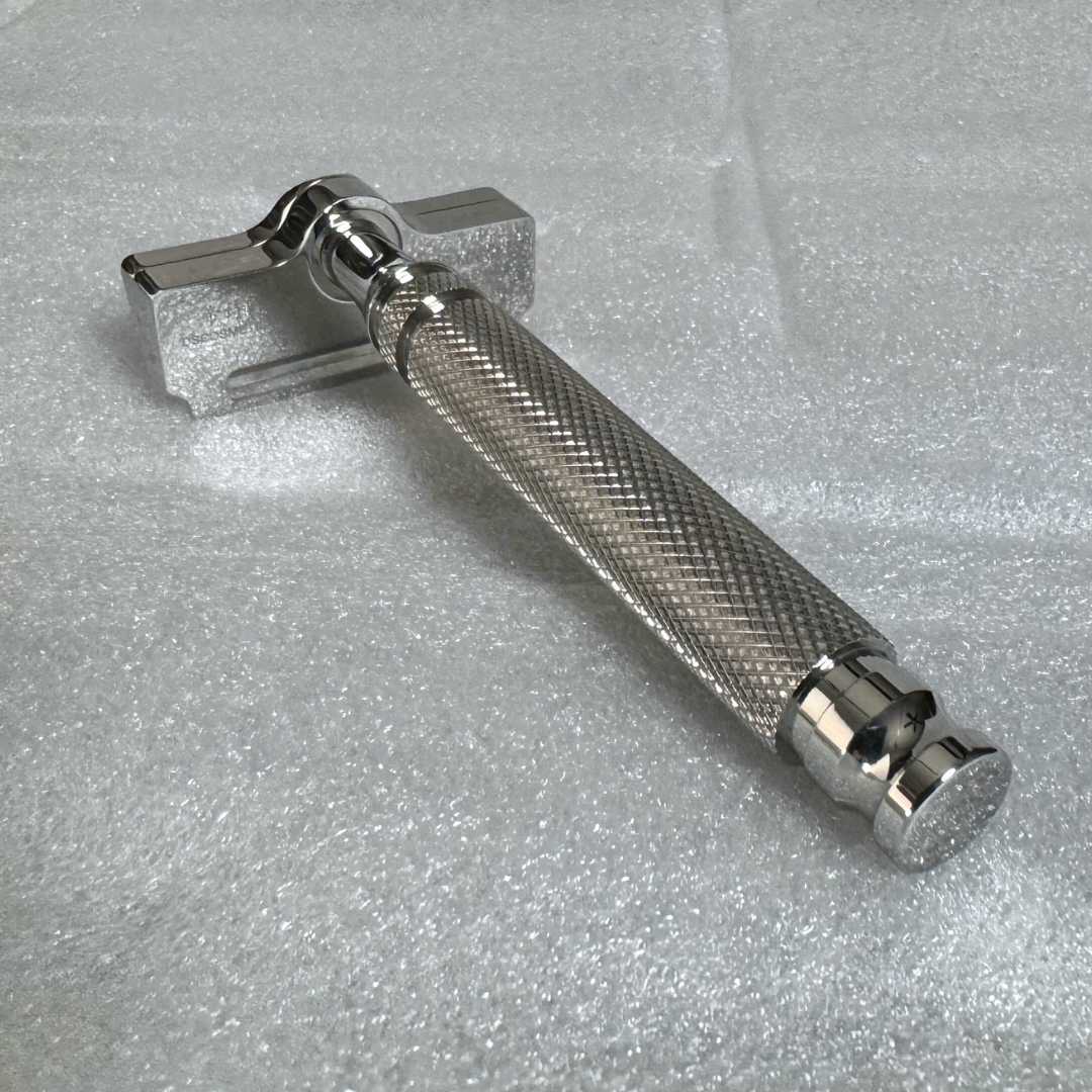Safety razor lying flat: chrome head, textured grip, and knurled handle end